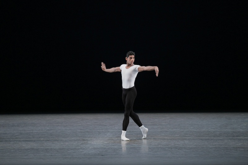 Ramasar dressed in black tights and white leo. His arms are spread wide and are hands are flexed